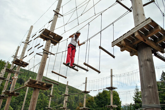 Young woman in a rope amusement park crossing a suspension bridge
