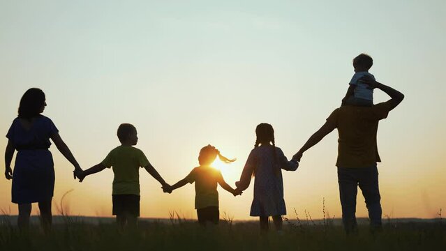 Happy family. Children with parents in park on grass. Family fun at sunset. Silhouette people are walk in park.Summer walk in park. Child holds hand of parents.Happy family concept.Free family in park