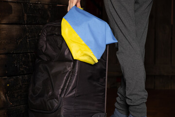 A Ukrainian woman with a suitcase and a flag of Ukraine leaves her home because of the war,...