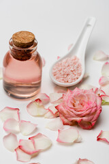 flower near petals, pink sea salt and bottle with rose water on white.