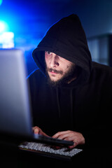 Vertical Portrait of mysterious hooded hacker sitting at desk and breaking into government data...