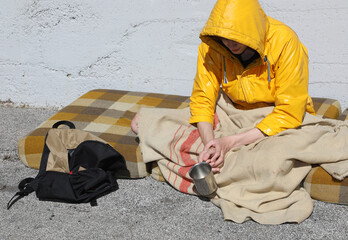 Poor beggar sitting on a filthy mattress in the street asking for charity and alms