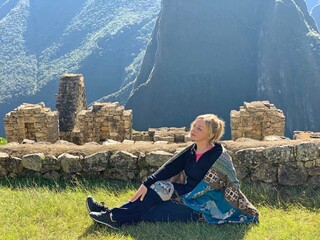 Blonde woman tourist in a Peruvian shawl sits on the lawn near Machu Picchu Pervu