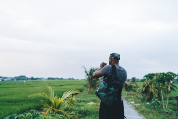 Back view of male videographer with touristic backpack using gopro camera equipment for shooting...