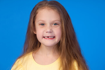 Toothless child. Cute little girl smiles broadly on a blue background. The first milk tooth fell out. The concept of pediatric dentistry and dental hygiene