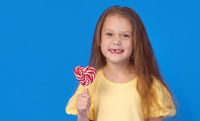 Toothless child. Cute little girl smiles broadly with lollipop  in hands. The first milk tooth fell...