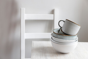 A pyramid of white bowls, plates and cups of different sizes and colors on a beige table in the kitchen. Scandinavian style. Place for your text. Copy space
