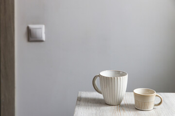 Two porcelain white cups are on the beige table. Large and small cup