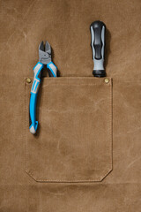Brown apron pocket with wire cutters or nippers and screwdriver. Selective focus