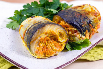 Homemade backed mackerel fish roll slices stuffed with carrots and onions with parsley for dinner on a plate in the kitchen. - 497781136