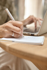 Close-up of a hand making a note. The laptop is running in the background. The concept of independent learning