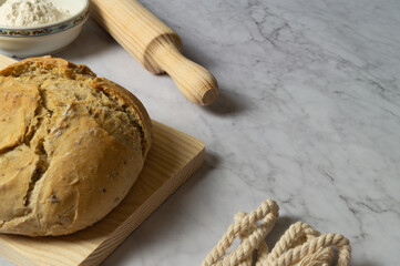 Loaf of sourdough bread on wooden board, freshly baked homemade, natural ingredients, freshness, flour, top photo, white marble background, space for text.