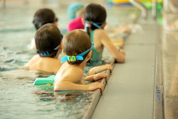 Obraz premium Child, taking swimming lessons in a group of children in indoor pool