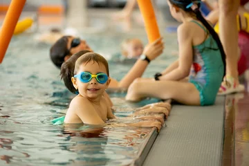 Fotobehang Child, taking swimming lessons in a group of children in indoor pool © Tomsickova