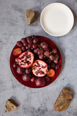 still life raw plums, pomegranate and grapes in a grey stone background
