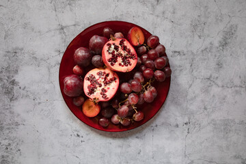 Obraz na płótnie Canvas still life raw plums, pomegranate and grapes in a grey stone background