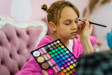 Little girl having a makeup treatment in children's spa center.