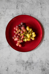 Still life dark and green grapes in on a red dish in a stone background