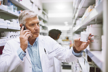We need more pain killers. Shot of a focused mature male pharmacist talking on his cellphone while...