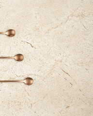Three coffee spoon, bronze color. Top view, flat lay. Beige marble background