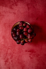 still life raw plums, pomegranate and grapes in a red stone background