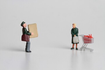 miniature figurines of a postman delivering a parcel to an old woman shopping with a supermarket cart