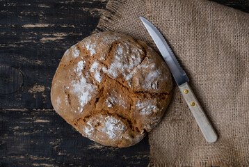 Fresh homemade bread with burlap napkin and knife on dark background. Top view. Rustic style