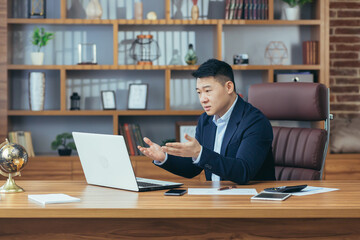 Asian businessman boss talking to colleagues on video call, looking at laptop screen, working in office, online meeting