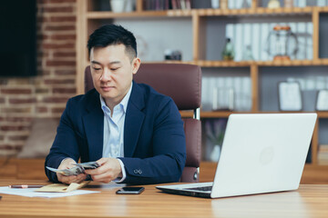 Obraz premium Successful asian businessman man counts american dollars cash, banker happy with profit