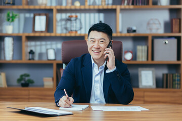 Successful paper boss in office looks at camera and smiles, asian businessman