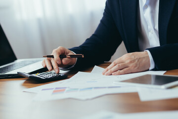 Close-up photo, businessman accountant's hand counts on a calculator, man sitting at a table paperwork