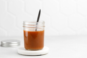 Delicious dessert caramel sauce in jar with spoon on white background. Homemade caramel in a glass jar.