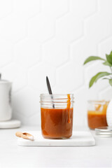 Homemade caramel in a jar with spoon. Salted Caramel sauce on white board, tile background