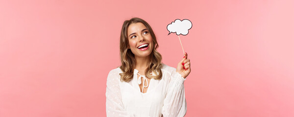 Spring, happiness and celebration concept. Dreamy and lovely blond girl daydreaming, saying something, holding comment cloud stick near mouth as if talking, look away daydreaming - obrazy, fototapety, plakaty