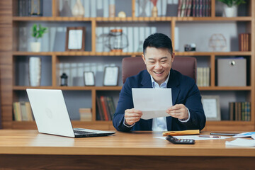 Portrait of a successful businessman, Asian received a letter of approval from the bank, to extend the credit line, a happy man working at the table, holding an envelope