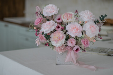 Beautiful bouquet of peonies and pink roses on the table. In the background is the interior of a modern white kitchen. Concept of home comfort.