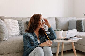 Stylish modern girl is glasses and denim shirt is working at home remote.