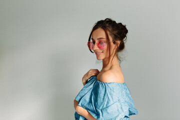 Beautiful lady in pink glasses and denim top is looking down and smiling on isolated background