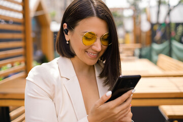 Lady in yellow sunglasses reads messages on phone while sitting in restaurant on the outdoors....