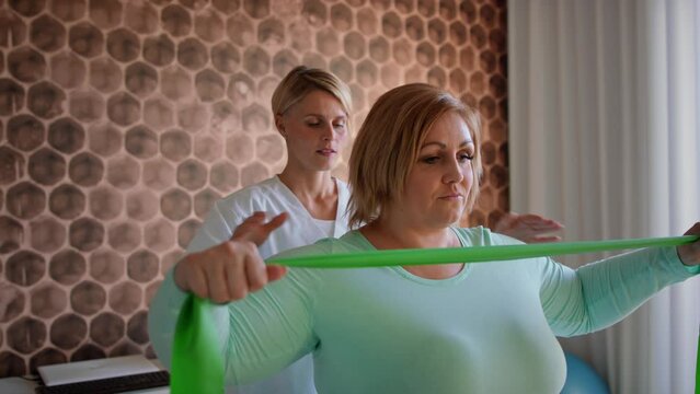 Physiotherapist woman exercising with overweight woman indoors in rehabilitation center