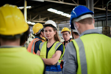 A confident, beautiful Caucasian woman worker stands among the male workers wearing safety uniform are meeting morning talk before the start of work in heavy industrial manufacturer factory.