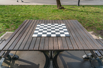Chessboard on a wooden table against the background of green grass in a city park in Krakow, Poland