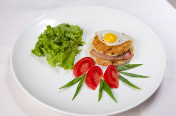 Sandwich with meat and egg, fresh green salad, fresh red tomatoes on a white bowl.