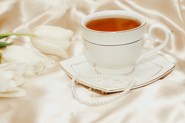 Bouquet of white tulips with pearl beads and tea on silk golden nude satin background.