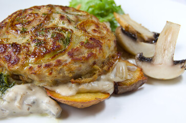Casserole with fried onion rings, meat, potatoes, sauce and mushrooms baked mushrooms. Leaf of fresh green lettuce.