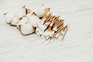 Cosmetic eco sticks on a cardboard base are scattered with cotton on a white background.