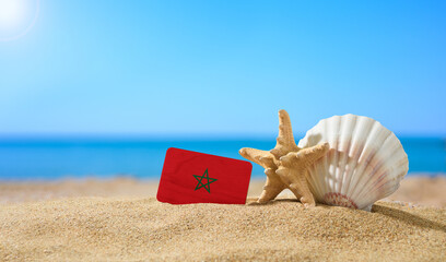 Fototapeta na wymiar Tropical beach with seashells and Morocco flag. The concept of a paradise vacation on the beaches of Morocco.