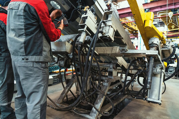 Workers at farm machinery factory assemble spare parts on special machine tool in workplace.