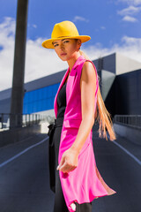 Fashionable girl on the background of a modern office building, trendy style, pink jacket and yellow hat