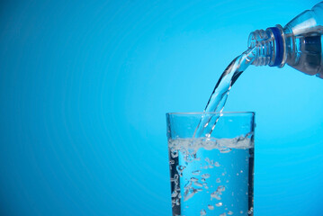 Pouring water into a glass against light blue background. fresh water a glass with bubbles blue...